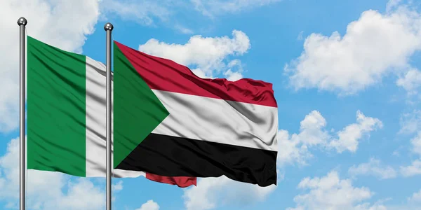 Bandera de Italia y Sudán ondeando en el viento contra el cielo azul nublado blanco juntos. Concepto diplomático, relaciones internacionales . — Foto de Stock