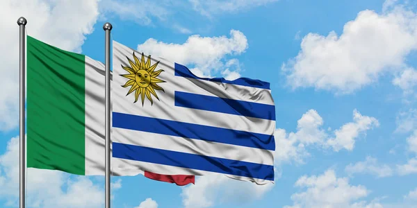 白い曇り青空に向かう風に揺れ、イタリアとウルグアイの旗が一緒に。外交概念、国際関係. — ストック写真