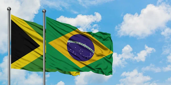 Bandera de Jamaica y Brasil ondeando en el viento contra el cielo azul nublado blanco juntos. Concepto diplomático, relaciones internacionales . — Foto de Stock