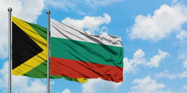 Bandera de Jamaica y Bulgaria ondeando en el viento contra el cielo azul nublado blanco juntos. Concepto diplomático, relaciones internacionales . — Foto de Stock