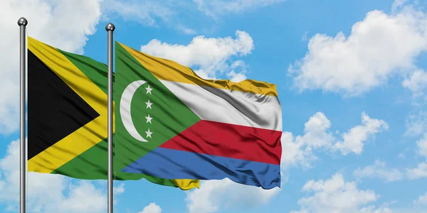 Jamaica e Comores bandeira acenando no vento contra o céu azul nublado branco juntos. Conceito de diplomacia, relações internacionais . — Fotografia de Stock