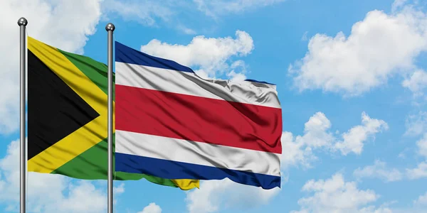 Giamaica e Costa Rica bandiera sventolando nel vento contro bianco cielo blu nuvoloso insieme. Concetto di diplomazia, relazioni internazionali . — Foto Stock
