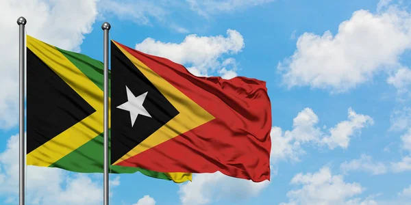 Jamaica y Timor Oriental ondean en el viento contra el cielo azul nublado blanco juntos. Concepto diplomático, relaciones internacionales . — Foto de Stock