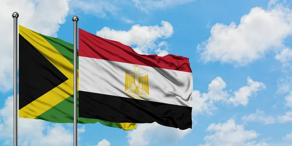 Bandera de Jamaica y Egipto ondeando en el viento contra el cielo azul nublado blanco juntos. Concepto diplomático, relaciones internacionales . — Foto de Stock