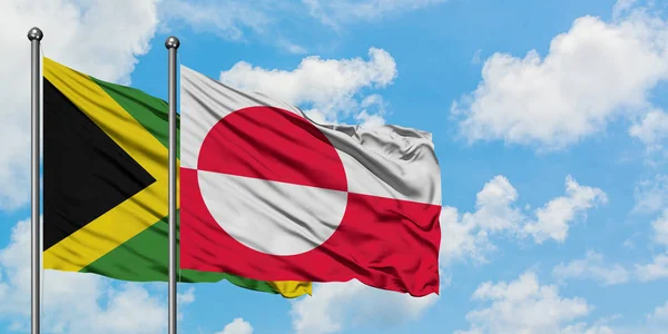 Jamaica y la bandera de Groenlandia ondeando en el viento contra el cielo azul nublado blanco juntos. Concepto diplomático, relaciones internacionales . — Foto de Stock