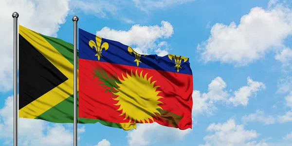 Bandera de Jamaica y Guadalupe ondeando en el viento contra el cielo azul nublado blanco juntos. Concepto diplomático, relaciones internacionales . — Foto de Stock