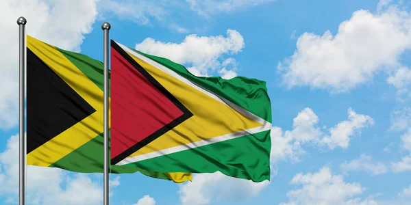 Bandera de Jamaica y Guyana ondeando en el viento contra el cielo azul nublado blanco juntos. Concepto diplomático, relaciones internacionales . — Foto de Stock