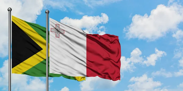 Bandera de Jamaica y Malta ondeando en el viento contra el cielo azul nublado blanco juntos. Concepto diplomático, relaciones internacionales . — Foto de Stock
