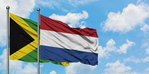Giamaica e Olanda bandiera sventolando nel vento contro bianco cielo blu nuvoloso insieme. Concetto di diplomazia, relazioni internazionali . — Foto Stock