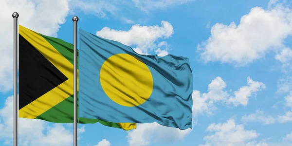 자메이카와 팔라우 깃발이 하얀 흐린 푸른 하늘을 배경으로 바람에 흔들리고 있습니다. 외교 개념, 국제 관계. — 스톡 사진
