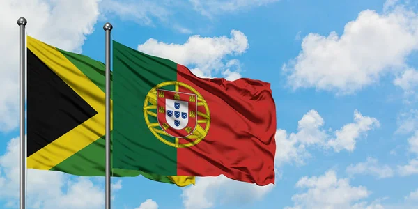 Bandera de Jamaica y Portugal ondeando en el viento contra el cielo azul nublado blanco juntos. Concepto diplomático, relaciones internacionales . — Foto de Stock