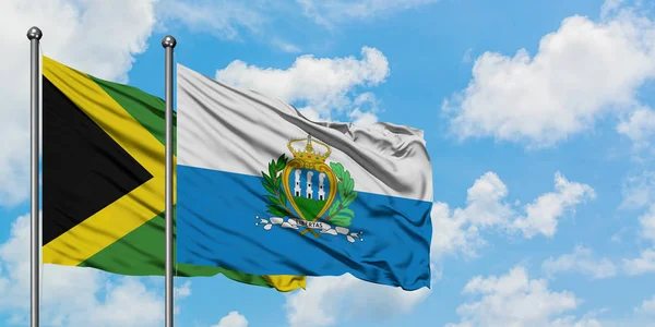 Bandera de Jamaica y San Marino ondeando en el viento contra el cielo azul nublado blanco juntos. Concepto diplomático, relaciones internacionales . — Foto de Stock