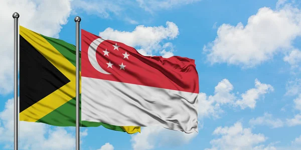 Bandera de Jamaica y Singapur ondeando en el viento contra el cielo azul nublado blanco juntos. Concepto diplomático, relaciones internacionales . — Foto de Stock