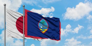 Japonya ve Guam bayrağı birlikte beyaz bulutlu mavi gökyüzüne karşı rüzgarda sallayarak. Diplomasi kavramı, uluslararası ilişkiler.