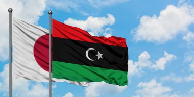 Japonya ve Libya bayrağı birlikte beyaz bulutlu mavi gökyüzüne karşı rüzgarsal sallayarak. Diplomasi kavramı, uluslararası ilişkiler.