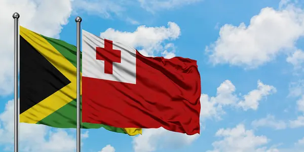 Bandera de Jamaica y Tonga ondeando en el viento contra el cielo azul nublado blanco juntos. Concepto diplomático, relaciones internacionales . — Foto de Stock