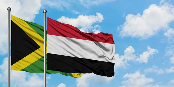 Bandera de Jamaica y Yemen ondeando en el viento contra el cielo azul nublado blanco juntos. Concepto diplomático, relaciones internacionales . — Foto de Stock
