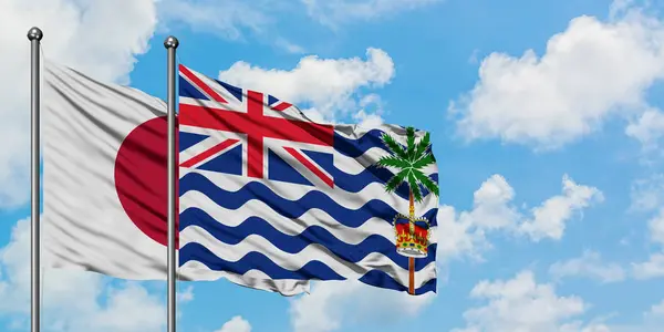 Bandera de Japón y del Territorio Británico del Océano Índico ondeando en el viento contra el cielo azul nublado blanco juntos. Concepto diplomático, relaciones internacionales . — Foto de Stock