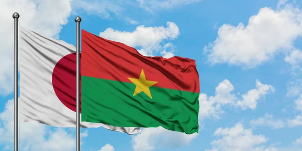 Bandera de Japón y Burkina Faso ondeando en el viento contra el cielo azul nublado blanco juntos. Concepto diplomático, relaciones internacionales . — Foto de Stock