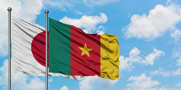 Bandera de Japón y Camerún ondeando en el viento contra el cielo azul nublado blanco juntos. Concepto diplomático, relaciones internacionales . — Foto de Stock