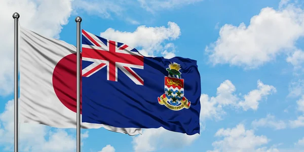 Japonya ve Cayman Adaları bayrağı birlikte beyaz bulutlu mavi gökyüzüne karşı rüzgarda sallayarak. Diplomasi kavramı, uluslararası ilişkiler. — Stok fotoğraf