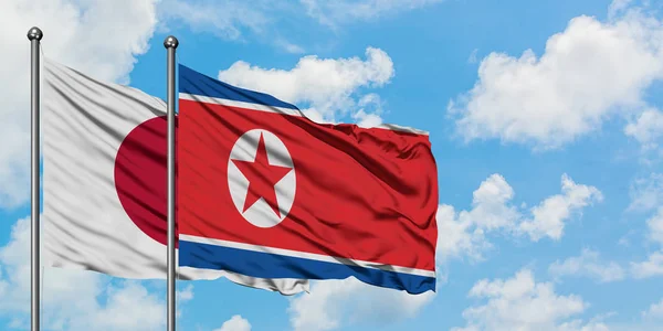 Η σημαία της Ιαπωνίας και της Βόρειας Κορέας κουνώντας τον άνεμο εναντίον του λευκού νεφελώδη μπλε ουρανού μαζί. Φιλοσοφία της διπλωματίας, διεθνείς σχέσεις. — Φωτογραφία Αρχείου