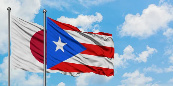 Japonya ve Porto Riko bayrağı birlikte beyaz bulutlu mavi gökyüzüne karşı rüzgarda sallayarak. Diplomasi kavramı, uluslararası ilişkiler. — Stok fotoğraf