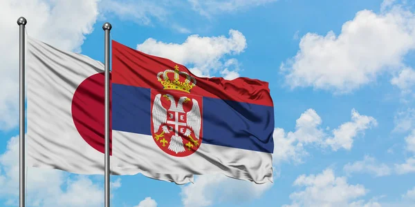 Bandera de Japón y Serbia ondeando en el viento contra el cielo azul nublado blanco juntos. Concepto diplomático, relaciones internacionales . — Foto de Stock