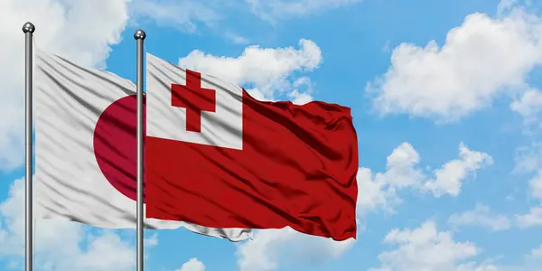 Bandera de Japón y Tonga ondeando en el viento contra el cielo azul nublado blanco juntos. Concepto diplomático, relaciones internacionales . — Foto de Stock