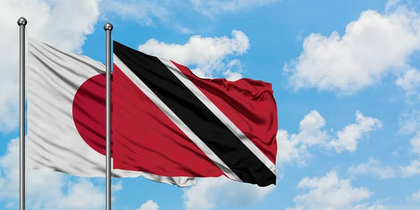 Japan en Trinidad en Tobago vlag zwaaien in de wind tegen witte bewolkte blauwe hemel samen. Diplomatie concept, internationale betrekkingen. — Stockfoto