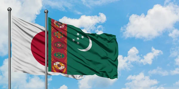 Bandera de Japón y Turkmenistán ondeando en el viento contra el cielo azul nublado blanco juntos. Concepto diplomático, relaciones internacionales . — Foto de Stock