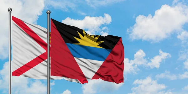 Jersey y Antigua y Barbuda bandera ondeando en el viento contra el cielo azul nublado blanco juntos. Concepto diplomático, relaciones internacionales . — Foto de Stock