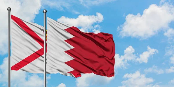 Bandera de Jersey y Bahréin ondeando en el viento contra el cielo azul nublado blanco juntos. Concepto diplomático, relaciones internacionales . — Foto de Stock