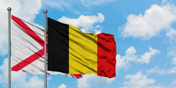 Jersey en België vlag zwaaien in de wind tegen witte bewolkte blauwe hemel samen. Diplomatie concept, internationale betrekkingen. — Stockfoto