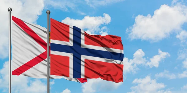 Bandera de Jersey y Bouvet Islands ondeando en el viento contra el cielo azul nublado blanco juntos. Concepto diplomático, relaciones internacionales . — Foto de Stock