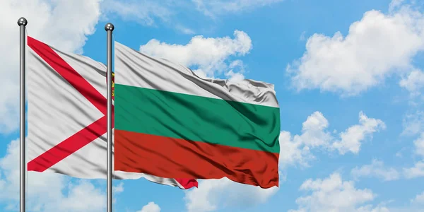 Bandera de Jersey y Bulgaria ondeando en el viento contra el cielo azul nublado blanco juntos. Concepto diplomático, relaciones internacionales . — Foto de Stock