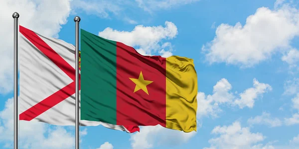 Bandera de Jersey y Camerún ondeando en el viento contra el cielo azul nublado blanco juntos. Concepto diplomático, relaciones internacionales . — Foto de Stock