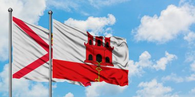 Jersey ve Cebelitarık bayrağı birlikte beyaz bulutlu mavi gökyüzüne karşı rüzgarda sallayarak. Diplomasi kavramı, uluslararası ilişkiler.
