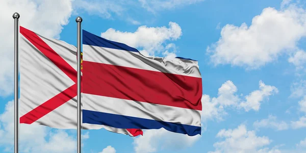 一緒に白い曇り青い空に対して風に手を振るジャージーとコスタリカの旗。外交概念、国際関係. — ストック写真