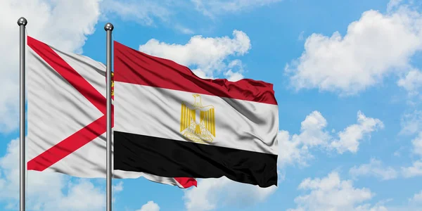 Bandera de Jersey y Egipto ondeando en el viento contra el cielo azul nublado blanco juntos. Concepto diplomático, relaciones internacionales . — Foto de Stock