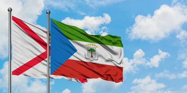 Bandera de Jersey y Guinea Ecuatorial ondeando en el viento contra el cielo azul nublado blanco juntos. Concepto diplomático, relaciones internacionales . — Foto de Stock
