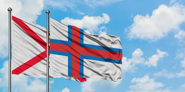 Джерсі і Фарерські острови прапор розмахуючи в вітру проти білого хмарного синього неба разом. Концепція дипломатії, міжнародні відносини. — стокове фото