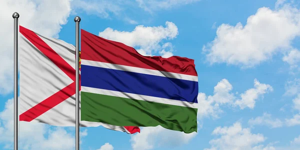 Jersey e Gambia sventolano nel vento contro il bianco cielo blu nuvoloso insieme. Concetto di diplomazia, relazioni internazionali . — Foto Stock