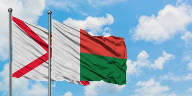 Jersey ve Madagaskar bayrağı birlikte beyaz bulutlu mavi gökyüzüne karşı rüzgarda sallayarak. Diplomasi kavramı, uluslararası ilişkiler.