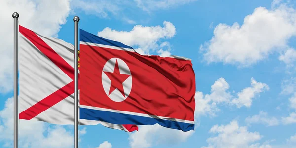 Jersey e la Corea del Nord bandiera sventolando nel vento contro bianco cielo blu nuvoloso insieme. Concetto di diplomazia, relazioni internazionali . — Foto Stock