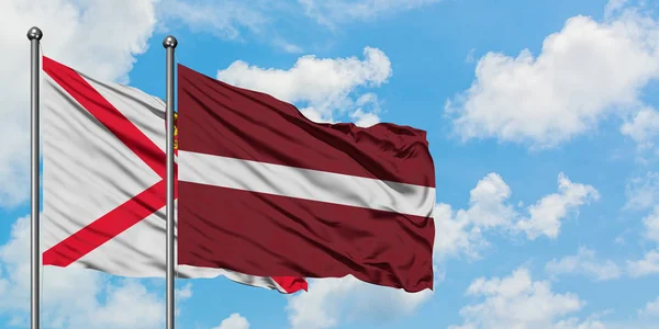 Jersey och Lettland flagga vifta i vinden mot vit grumlig blå himmel tillsammans. Diplomatisk koncept, internationella relationer. — Stockfoto