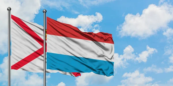 Jersey i Luksemburg flagi machając w wiatr przed białym zachmurzone błękitne niebo razem. Koncepcja dyplomacji, stosunki międzynarodowe. — Zdjęcie stockowe