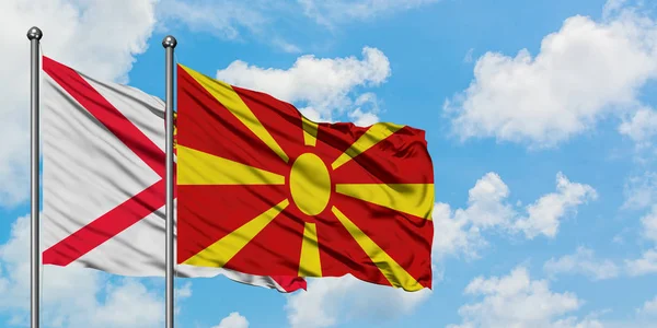 Jersey e Macedônia bandeira acenando no vento contra o céu azul nublado branco juntos. Conceito de diplomacia, relações internacionais . — Fotografia de Stock