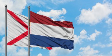 Jersey ve Hollanda bayrağı birlikte beyaz bulutlu mavi gökyüzüne karşı rüzgarda sallayarak. Diplomasi kavramı, uluslararası ilişkiler.