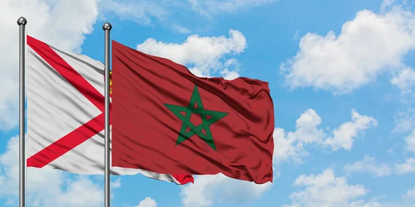 Bandera de Jersey y Marruecos ondeando en el viento contra el cielo azul nublado blanco juntos. Concepto diplomático, relaciones internacionales . — Foto de Stock